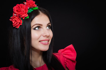 Woman with long black hair and wreath with red flowers on a dark background smiles. Close-up. Space for text
