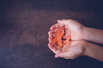 Hands holding Orange Ribbons on toning background, Leukemia awareness, Self Injury Awareness Day,...