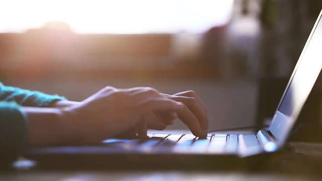 Woman hands working indoors on a laptop with beautiful sunset light in background