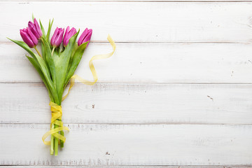 Spring purple tulips with yellow ribbon on white wooden boards, top view
