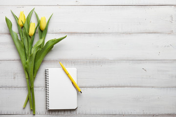 Spring yellow tulips and notebook with pen on white wooden boards, top view