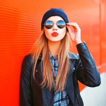 Fashion portrait beautiful blonde woman sends air kiss blowing red lips outdoors wearing sunglasses and hat