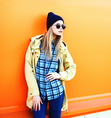 Fashion portrait blonde woman in black sunglasses hat posing on a colorful orange background