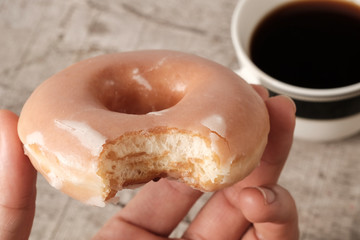 Hand holding bite missing glazed donut
