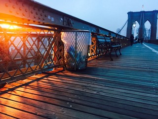trash and bench on walkway at Brooklyn bridge with fog before night in vintage colorful style