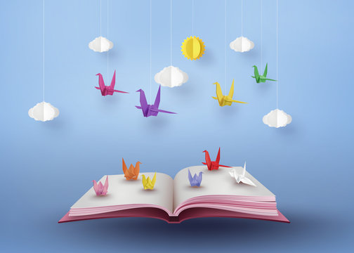 origami made colorful paper bird flying over open book
