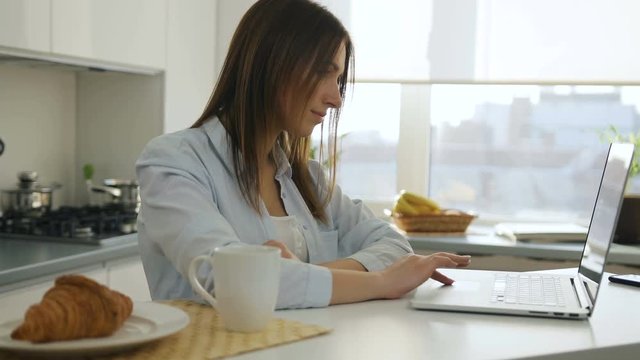 Young woman browsing something on her laptop and drinking coffee