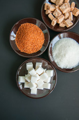Variety of brown (cane) and white sugar. Granulated and lump sugar in a black small plates. 