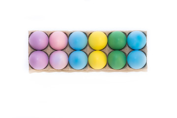 A dozen colored Easter eggs dyed lavender, pink, blue, yellow and green in a cardboard cartoon from above on a white background with copy space.