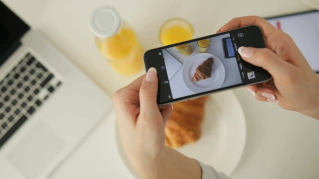 Woman taking picture of croissant and orange juice in the kitchen by smart phone