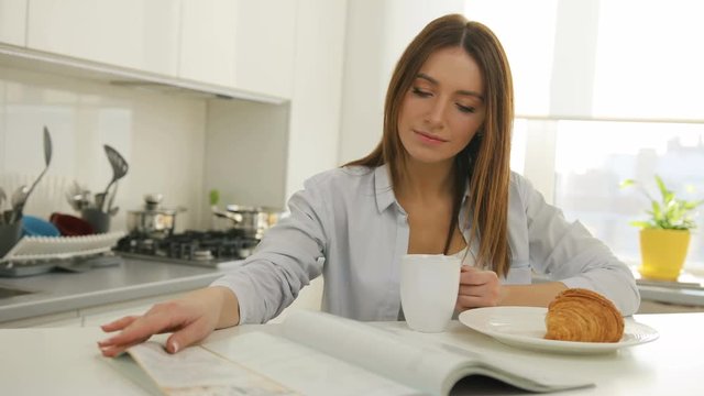 Young woman thumbing through the magazine in the kitchen.