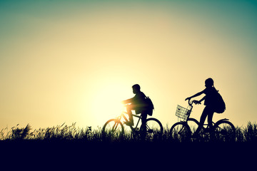 Fototapeta na wymiar Silhouette of children with bicycle on grass field at the sky sunset, color of vintage tone and soft focus concept journey in holiday