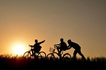 Fototapeta na wymiar Silhouette of family with bicycle on grass field at the sky sunset, color of vintage tone and soft focus concept journey in holiday