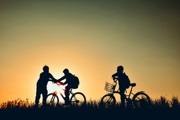 Obraz premium Silhouette of family with bicycle on grass field at the sky sunset, color of vintage tone and soft focus concept journey in holiday