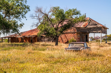 Overgrown field with an abandoned car and an old gas station and motel