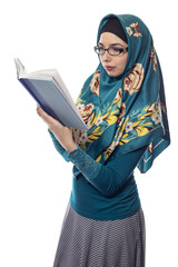 Female foreign exchange student wearing glasses and a hijab reading a text book.  The conservative...