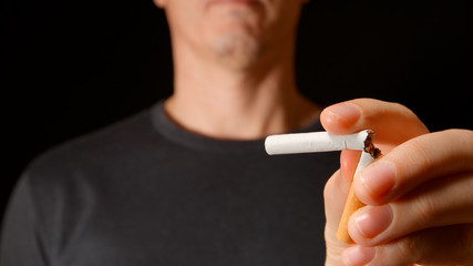 Young adult man holds a broken cigarette at hand