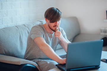 A bearded man with a laptop sitting on the sofa at home