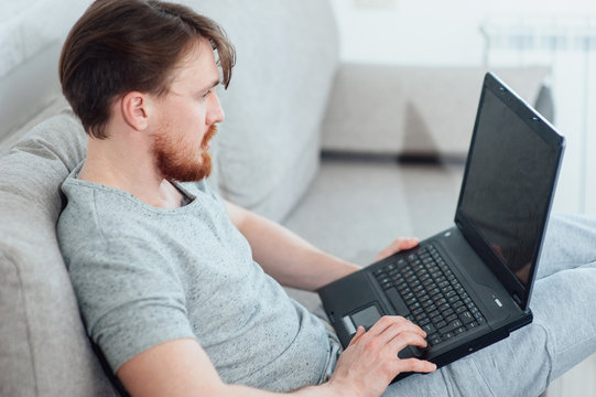 A bearded man with a laptop sitting on the sofa at home