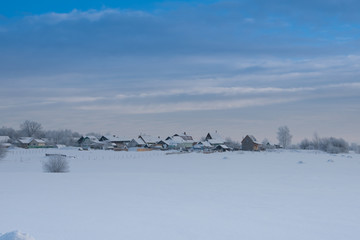 Winter photo of the village on the background of snowy fields and blue sky