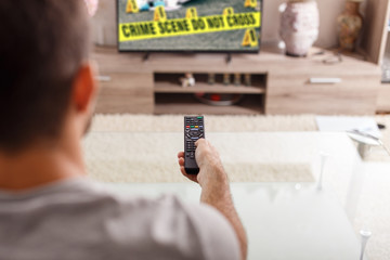 Man with remote control watching crime serie in TV