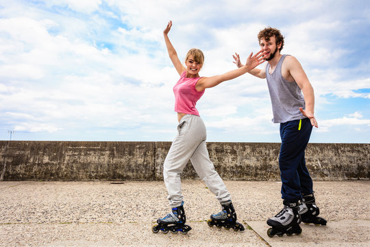 Two people on rollerblades with spread arms.