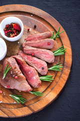 Roast beef steak on a wooden cutting board with rosemary, top view. Grilled meat closeup