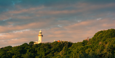 Fototapeta na wymiar Byron Bay lighthouse view from the distance in a bright sunset light with cloudy sky, Australia