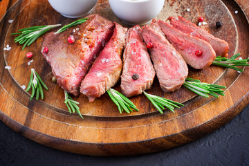 Roasted beef steak cut into slices with rosemary on wooden cutting board