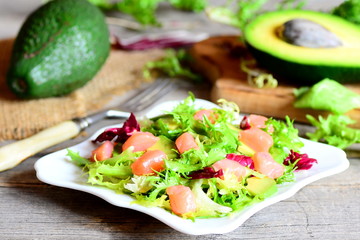 Homemade salad with red fish, lettuce mix, avocado, olive oil and lemon juice on the plate. Fresh raw avocado, fork on a wooden table. Vintage style. Closeup