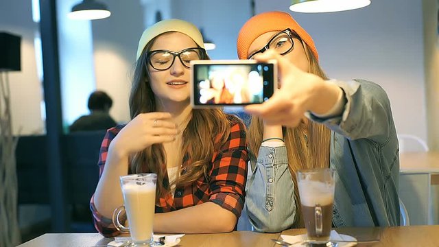 Hipster girls are doing photo of themselves on smartphone in the cafe
