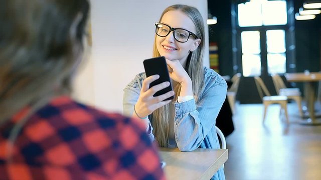 Blonde girl in denim shirt is doing selfies on smartphone during her meeting with a friend
