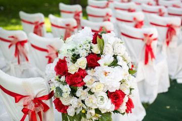 Wedding ceremony outdoors. White chairs with red ribbon.