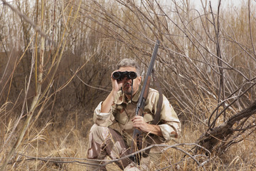 Hunter with shotgun looking through binoculars