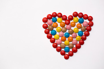 Colorful m&m button chocolate candies in the love shape on white background.