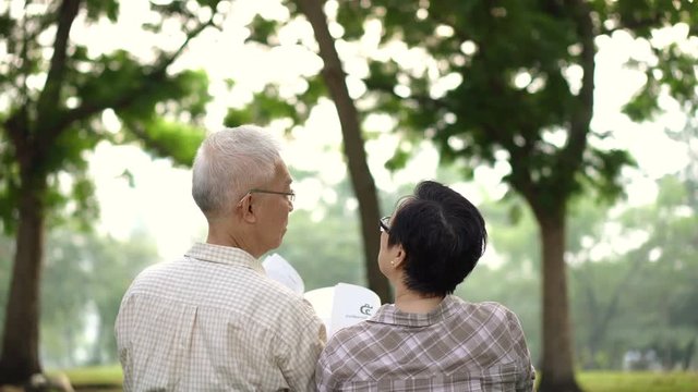 Back view of Asian senior couple sitting in park. Reading book together in relax asmosphere