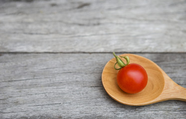 Fresh small tomato on wooden spoon over wood background