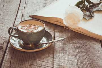 Cup of black coffee and open book with white rose on wooden board. Vintage toned. Close up.