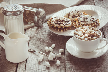 Fototapeta na wymiar White cup of coffee with milk, marshmallow and homemade waffle with whipped cream with decor on top. Tasty breakfast. Vintage toned.