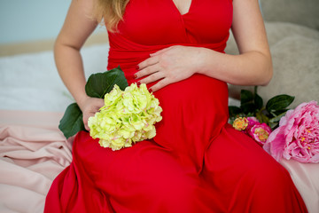Close-up Image of pregnant woman touching her belly with hands. Keeps yellow flowers in hand. Horizontal