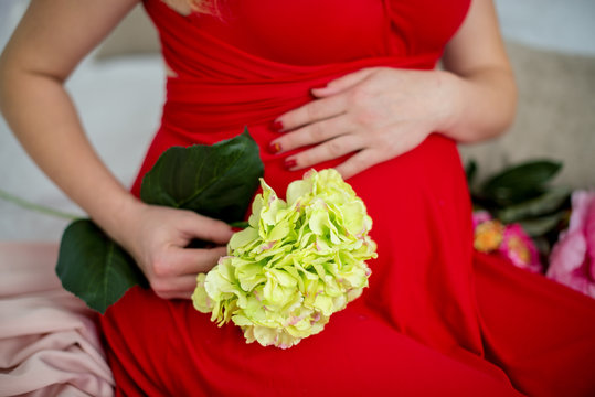 Close-up Image of pregnant woman touching her belly with hands. Keeps yellow flowers in hand