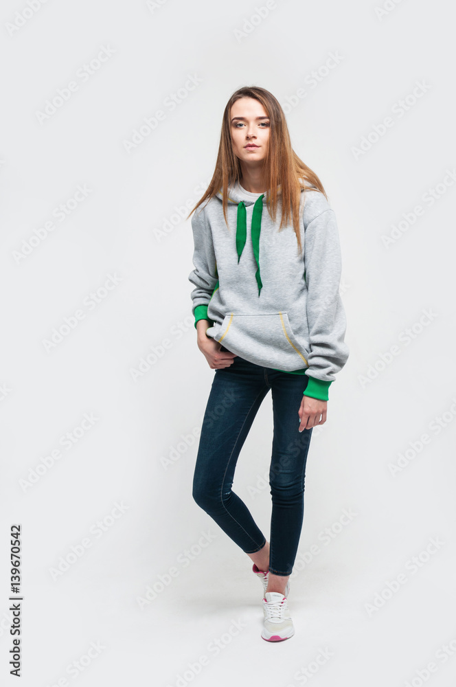 Wall mural Portrait of a cute positive blonde woman in a hoodie on grey background in studio