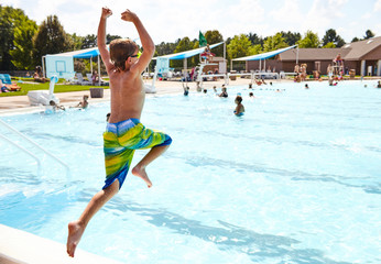 Energetic boy jumping in outdoor swimming pool