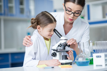 Teacher and little student scientists working with microscope in laboratory