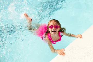 Happy little girl swimming holding on to pool edge