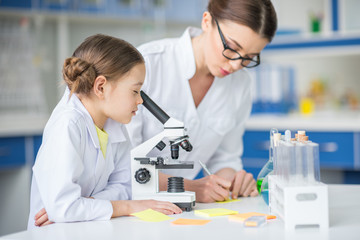 Teacher and student scientists working with microscope in laboratory