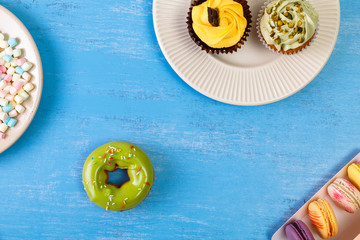 Cupcakes with buttercream. Macaroons in box and donut. Cake with pistachio nuts cream and small chocolate bar. Dessert with topping.