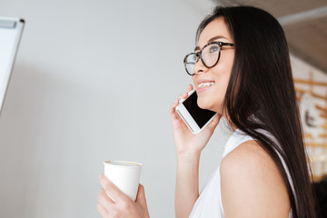 Cheerful woman drinking coffee lattee and talking on cell phone