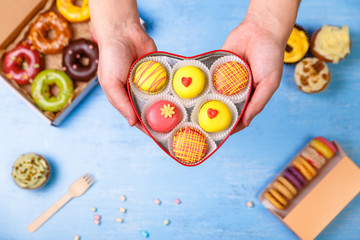 Macaroons, cupcakes and donuts. Male hands holding heart-shaped box. Cakes with buttercream. Almond macaron cookies. Sweet dessert.