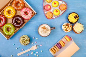 Macaroons, cupcakes and glazed donuts. Mug with whipped cream and cinnamon. Almond macaron cookies. Sweet dessert.